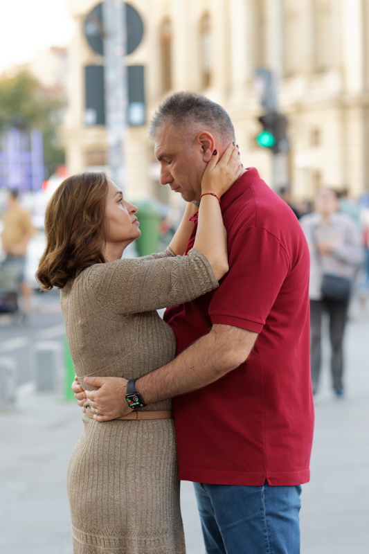 1 - A man in a red polo shirt and jeans embracing a woman wearing a gold-textured knit dress on a city street
